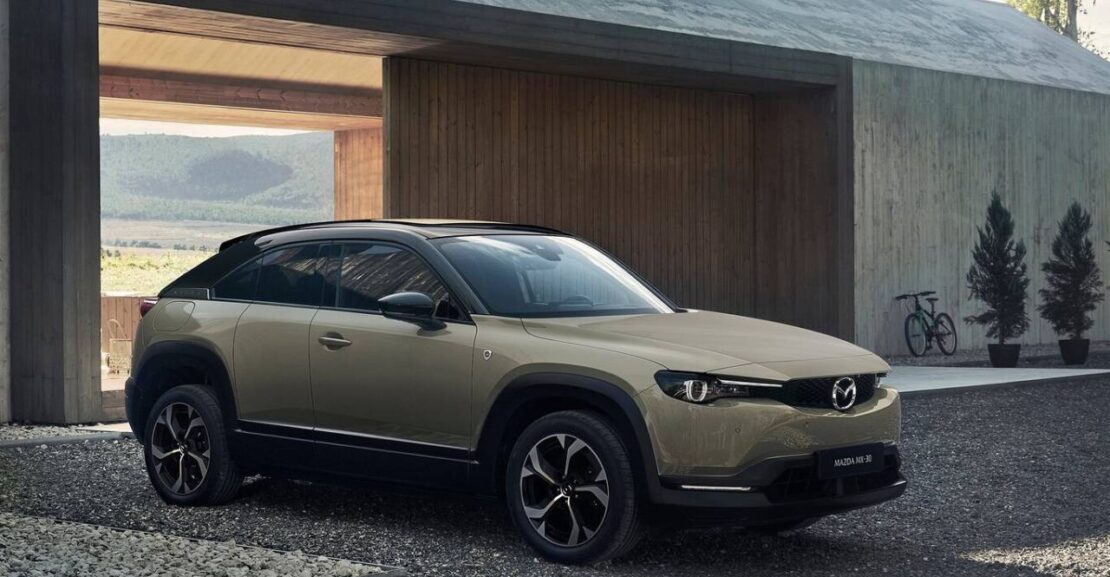 Mazda MX-30 de color beige, aparcado enfrente de una casa