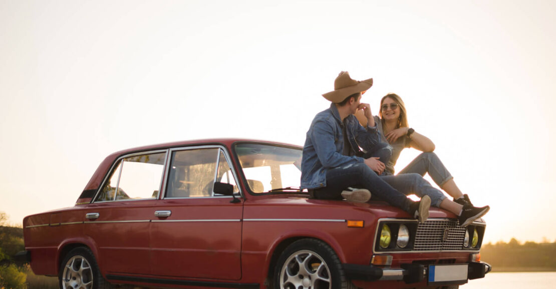 Una pareja charla encima del capó del coche clásico