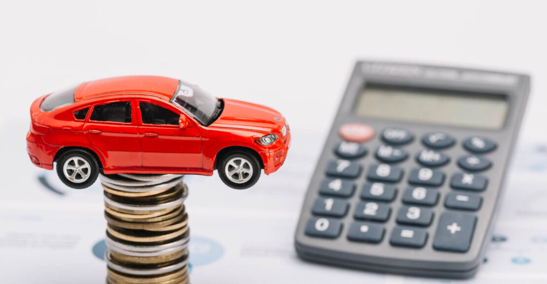 Un coche en lo alta de una torre de monedas junto a una calculadora.