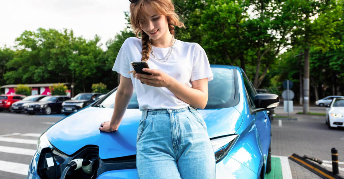 Una chica mira el móvil mientras se carga el coche eléctrico